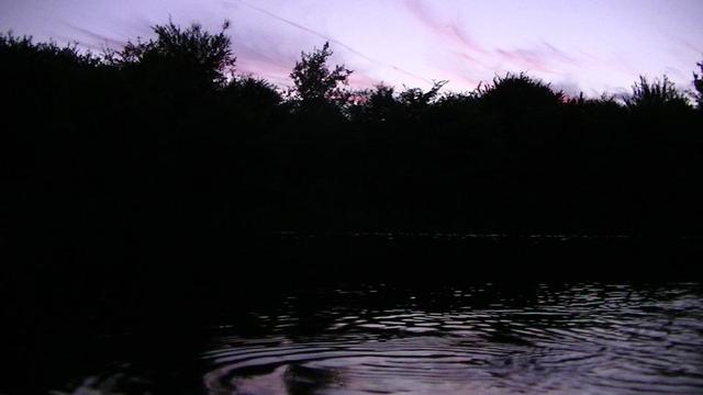purple sky at dusk. silhouette off trees on bank of lake. sky reflects in ripples on lake.
