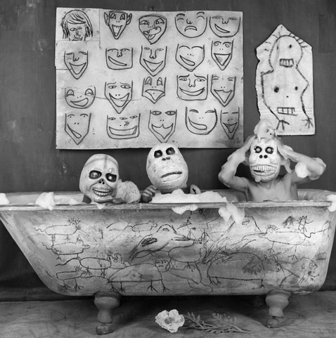 bubble bath by roger ballen. skeletal spirits chilling together, various faces hung up on the wall, flower on the floor