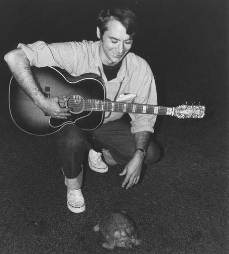 John Fahey kneeling with guitar to inspect a turtle