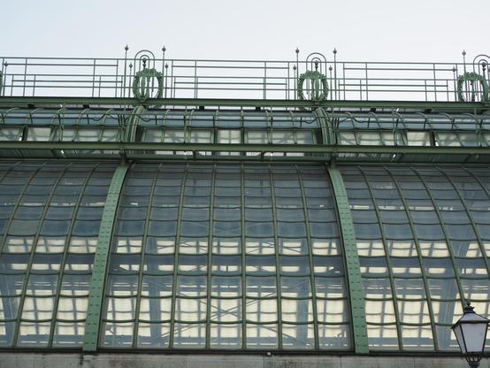 Das gewölbte Dach eines alten Glashauses mit grünen Metallstreben.