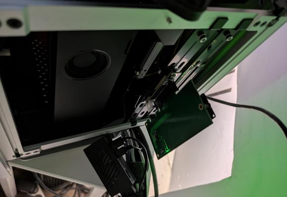 An Apple PCIe AHCI SSD in a carrier hanging off a PCIe x4 port bolted to the back of a weird cube-shaped computer
