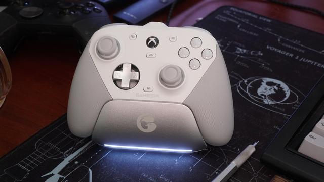 The GameSir G7 Pro Tri-Mode controller (white) charging in it charging station.  The station has an LED bar on the bottom that slowly flashes white while charging and turns off once the controller is charged.