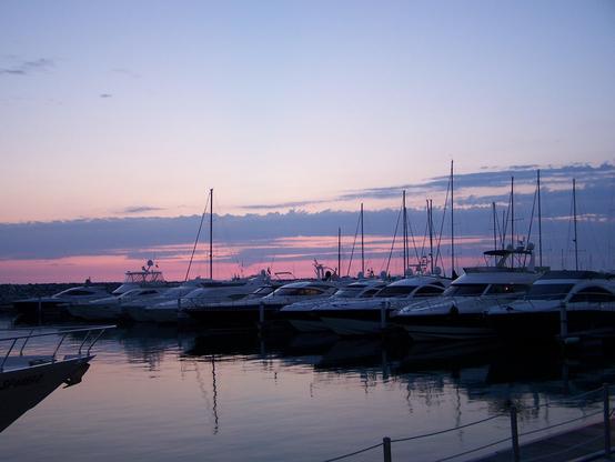 Viele Yachten im Hafenbecken, rosa Sonnenuntergangs-Himmel mit einigen Wolken quer durch das Bild.