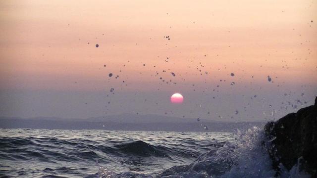 sunrise above a mountain from a rocky sea shore. wavedrops splashing into the sky above the sun