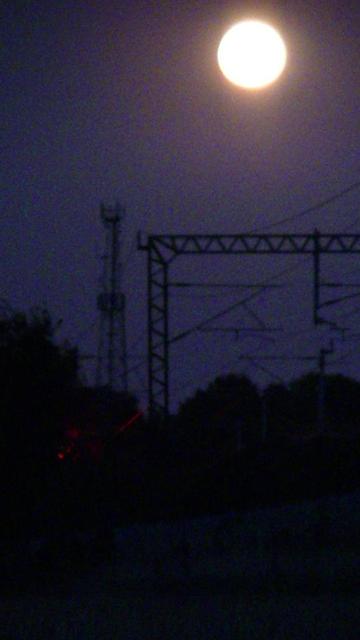 full moon over electrified railway at night. trace of rear red light of train i think might be signal too. blurry