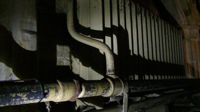 a Victorian cast iron radiator with iron pipework in a dark corner of the church under a low arched alcove