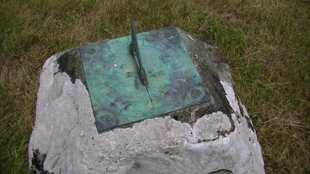 an old brass sundial on top of an ancient stone covered in white lichen