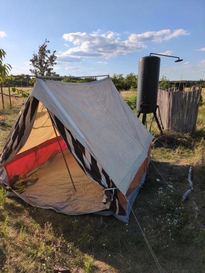 Altes Zelt in klassischer Bauweise, auf einer Wiese. Dahinter eine Outdoor dusche
