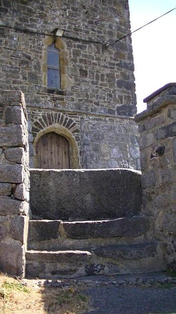 a normanish arch door of a 14th century stone church, lower part obscured by a upright flagstone style thingy for stepping over, i can't remember what they are called. the church was restored in 1839-1841. (St Ffraid's church, Ceredigion). the leaded window above the door is in view too. i will prolly toot a snap of the window from the inside for #windowFriday