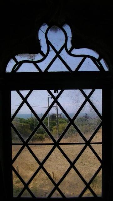 looking west out of a keel arch leaded window. view of the sea, trees, pair of wooden electricity poles holding transformer and cables. the window is above the door of St. Ffraed's church i tooted earlier for #doorsDay