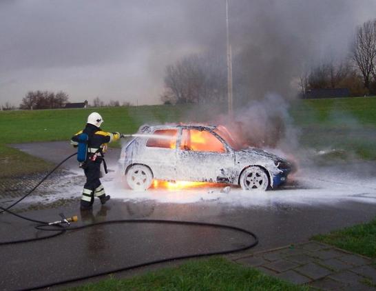 a firefighter spraying a burning car, smoke blowing up in the sky