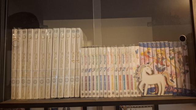 Vemos uma prateleira voadora cheia de coisas referentes à Sailor Moon. À direita a edição de luxo do mangá, no meio a edição convencional e à esquerda os DVDs (estes formando um mosaico com os principais personagens da franquia). Temos ainda um segurador de livros que não é da Sailor Moon mas que é um unicórnio colorido e por isso combina demais com a temática.