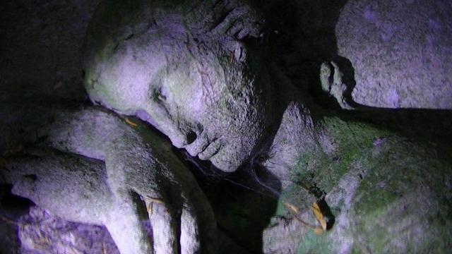 a carving of a girl resting on an arch doorway to a graveyard eyes closed, in torchlight, cobweb and spider under chin.