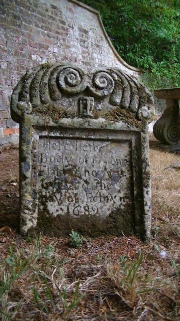 a grave stone with scroll like symmetric spirals on top. moss and lichen.
i use underscores for the unreadable weathered parts:
"Here lieth ___
body of ______
_____ of Feb__
      1689"