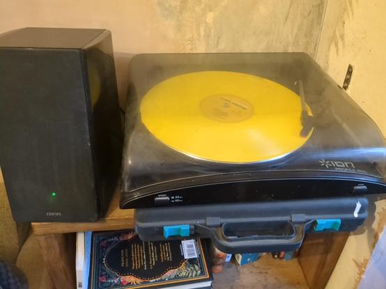 Slightly grimy turntable balanced on a miniatures case. Yellow Ned's Atomic Dustbin record spins on top