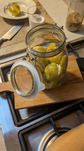 Foto af et henkogningsglas som står åben. I den ligger der en håndfuld citroner der er blevet fyldt med salt.