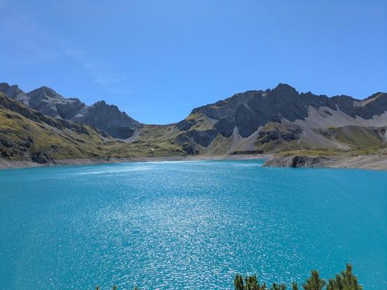 A lake with bright blue color in the foreground and some mountains in the background.