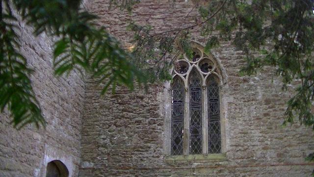 from beneath a yew tree looking at the west wall to the right of the tower of a limestone rubble, medieval st.Mary's church. there is an arched window containing three stained glass arches topped with three quatrefoils. that window is slightly misshaped with age. it had quite a few cobwebs too. i done a snap of them too but it was a bit blurry. more blurry than usual. s'pose a could toot it for #shittember. maybe later....