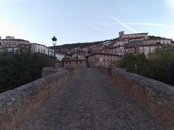 Foto de Villoslada de Cameris sacada desde el puente medieval. Al fondo del puente se ve la casa de piedra del ayuntamiento y el resto del pueblo en la ladera de la montaña