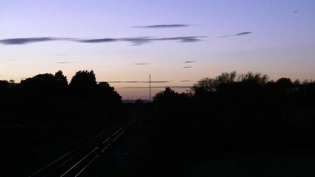 view from the bridge at dusk purple sky fading to orange on the horizon. railway beneath. small transmitter in the distance.