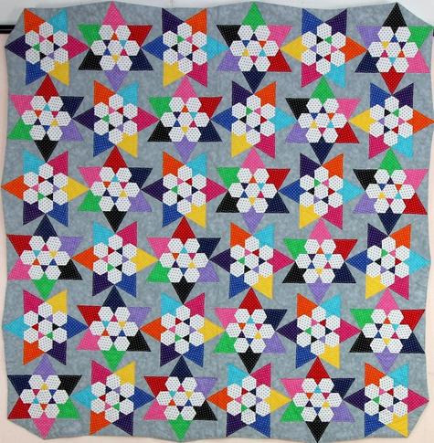 Eine bunte Patchwork-Decke, das Muster sind regelmäßig angeordnete Sternen auf grauem Hintergrund.