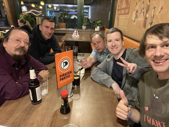 5 Männer in einem Wirtshaus, sie blicken in die Kamera. Am Tisch ein Wimpel der Piratenpartei.