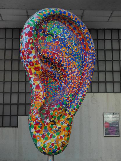 Eine Skulptur eines menschlichen Ohres, ca 3 Meter hoch, die Oberfläche ist mit einem bunten Mosaik dekoriert.