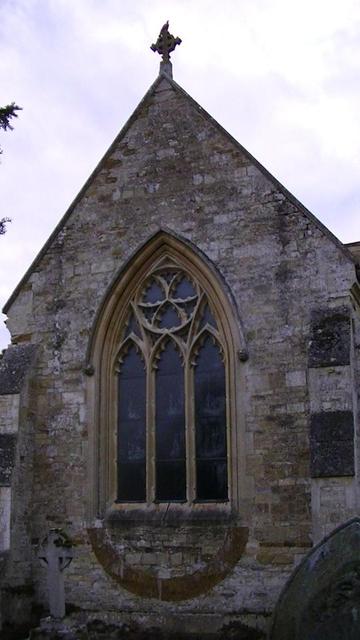 east chancel window of a medieval limestone rubble church. looks like the widow has been restored recently.  it has a pointy arch with trefoil and three-light arches beneath. it has an bowl shaped ironstone arch that has been filled in beneath the window. it's like a smile, lol. and there is a stone celtic cross on the ridge of the gable end.