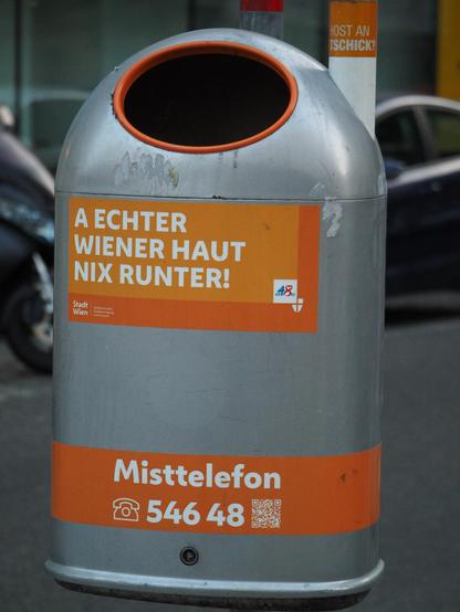 Ein öffentlicher Mülleimer in Wien mit einem Aufkleber "A echter Wiener haut nix runter!" und ein zweiter mit "Misttelefon" gefolgt von einer Telefonnummer. Es gibt 'zig verschiedene Aufkleber/Sprüche. 
