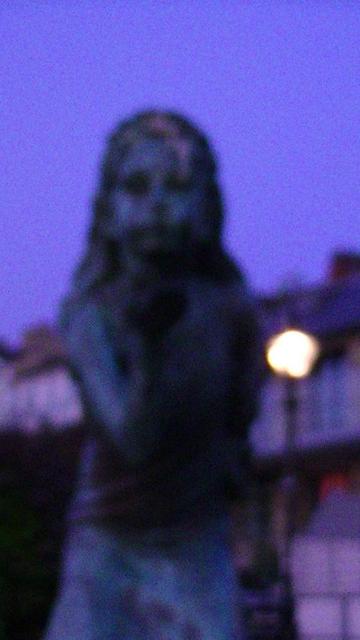a blurry and noisy snap of a bronze statue. it is supposed to be a girl blowing a kiss or something from her hand but this snap is so shit it could be anything.