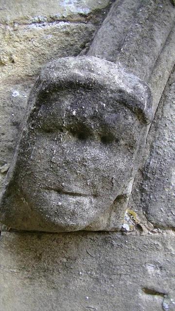 a crude carving of a head limestone label stop on a medieval church. odd bits of lichen. eyes are just 2 indents close together. the slight grin looks convincing though.