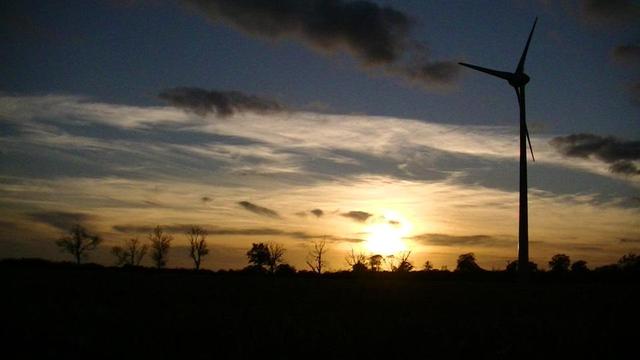 sun about to set. silhouette of a row of trees and a wind turbine on the right.
some whispy clouds. some low some higher in the atmosphere. orange. dark blue.