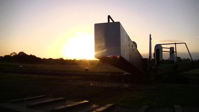 the sun setting to the left of a canal lock gate beam looking end on. horizon pretty flat with trees 