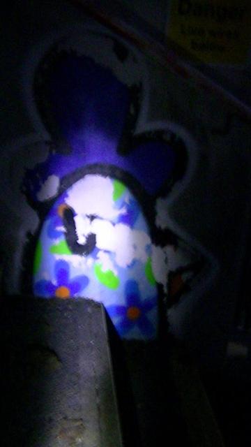 a flaking graffitied sleeping chickens head in torchlight,  on the wall of a steel footbridge stairwell, in the dead of night.