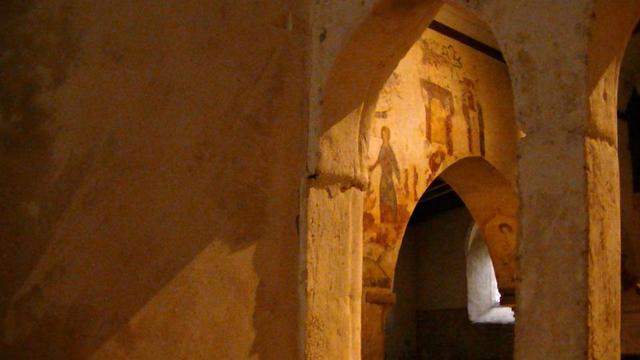 view from the chancel through small arches at more paintings. one is a lady holding a figure in some scales - "the weighing of the souls scene you can just make out the image of St George in his armour."