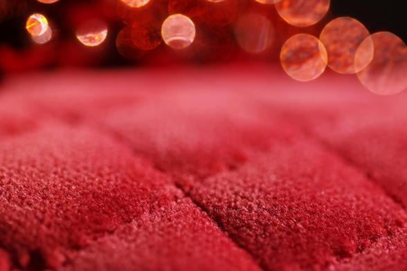 Ein Stück roter abgesteppter Samtstoff, im Hintergrund einige Unschärfekreise (bokeh) auch in rot 
