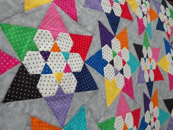 Die Oberseite von einem handgenähten Patchwork-Quilt mit 6eckigem Sternenmuster. Die meisten Stoffstücke sind mit Tupfen bedeckt.